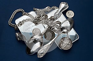 A handful of silver bullion, silverware, jewelery and old silver coins on a dark blue background