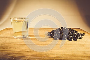 A handful of sunflower seed, sunflower oil in a glass on the table. Side view