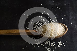 A handful of white polished rice in a wooden old spoon. Dark wood background.