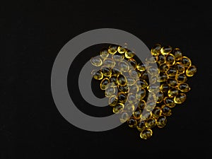 A handful of yellow pills in the shape of a heart on a black background. View from above. Copy space.