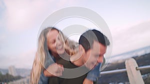 Handheld shot of a cheerful friend jumps on her friend`s back for piggyback ride on street, they laugh in natural way -