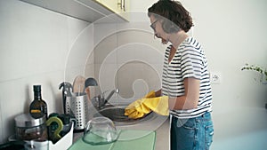 A handheld shot of a cheerful woman in yellow rubber gloves washes dishes