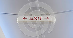 Handheld shot of overhead exit sign with left and right arrows inside an airplane, usually located near wing emergency exits.