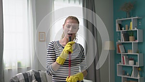 Handheld shot of young woman singing a song using a mop as a microphone