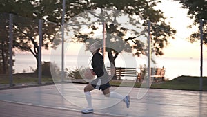 Handhelded footage of a young girl basketball player training and exercising outdoors on the local court. Dribbling with