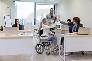 Handicap business woman giving high-five to colleague in creative office. Office workers and woman in a wheelchair are making a co