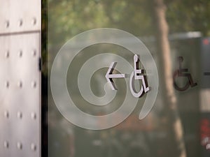 Handicap disabled wheelchair logo pointing to left outside steel wall on building