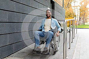 Handicapped accessible city. Positive impaired Afro man in wheelchair leaving building on ramp outdoors in autumn