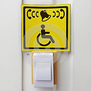Handicapped call button and yellow sign with icon on white wall