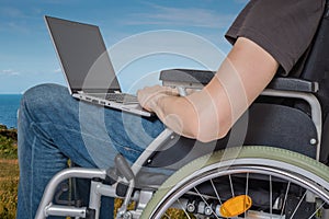 Handicapped disabled man on wheelchair is working with laptop outside