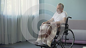 Handicapped pensioner sitting in wheelchair and thinking about life, sadness