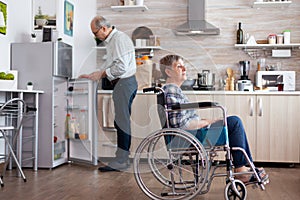 Handicapped senior woman in wheelchair sitting in kitchen looking throug window