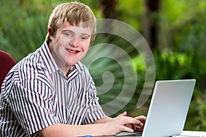 Handicapped young man typing on laptop in garden.