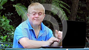 Handicapped young man typing on laptop in garden.