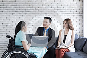 Handicapped young woman talking with colleagues using laptop computer in office. Disabled business executive on wheelchair using l