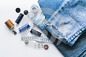 Handicraft, clothing repair. Ripped blue jeans sewing accessories white background. The concept of economical things.