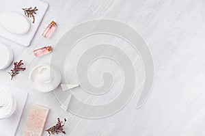 Handicraft natural cosmetics - white cream, soap, clay, rose oil, towel, pink flowers and bath accessories on soft light white.