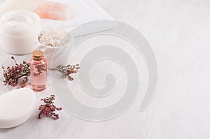 Handicraft natural cosmetics - white cream, soap, clay, rose oil, towel, pink flowers and bath accessories on soft white wood.