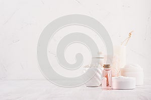 Handicraft natural cosmetics - white cream, soap, clay, rose oil, towel, pink salt and bath accessories on white wood board.