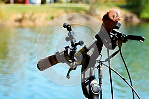 Handlebars of a pedelec with attachments for an action cam in front of the blurred background of a blue water with green shore