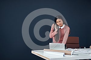 Handling business on all fronts. Shot of an attractive young female architect making a phone call while working in her