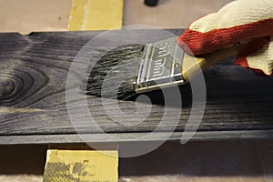 Handling a woody pine plank with a dark mordant with a paintbrush for deeply impregnating wood for painting purposes.