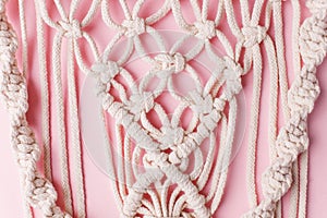 A handmade 100% cotton macrame wall decoration hanging on pink wall. Decoration for the interior. Trendy handcrafted decor for