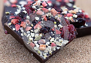 Handmade bitter chocolate with berries and green pistachios on a cork wood background. Macro photography of food. A close-up