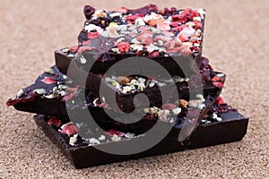 Handmade bitter chocolate with berries and green pistachios on a cork wood background. Macro photography of food. A close-up of a