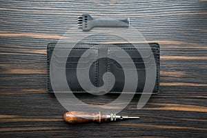 Handmade black leather wallet, punch and awl on a wooden table.