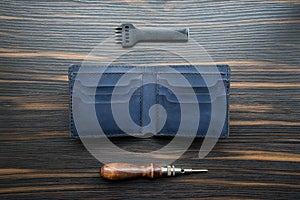 Handmade blue leather wallet, punch and awl on a wooden table.