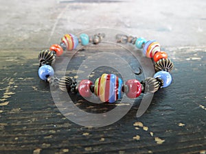 Handmade bracelet made from lampwork and glass beads on shabby wooden background. Boho handmade jewelry making concept