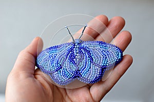 Handmade brooch of blue moth embroided with beads on a hand