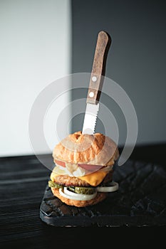 Handmade burger with beef, pickles, cheese and knife on black wooden board and table.