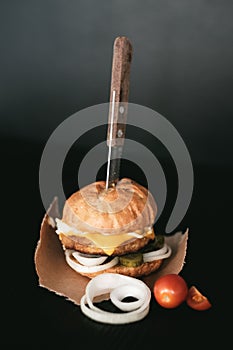 Handmade burger with beef, pickles, cheese and knife on black wooden table.