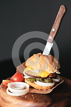 Handmade burger with beef, pickles, cheese and knife on wooden board.