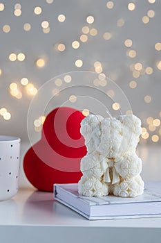 Handmade candle in the shape of teddy bear on white table with red heart. Valentine's day present