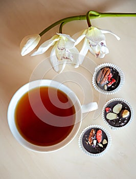Handmade chocolate with fresh and dried fruits and cup of hot tea on light wooden table