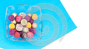 Handmade chocolate truffles, different colors on a platter on a blue and white background.