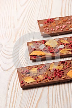 Handmade cholate bars whith mango, coconut and raspberry on white wooden table.