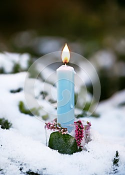 Handmade Christmas candle holder made of ice, pink calluna blossom branches with burning blue candle in the snow covered garen.