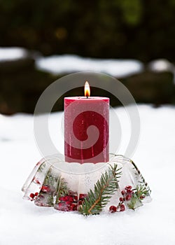 Handmade Christmas candle holder in shape of cake made of ice, red rose hips berries, holly berry branches and thuja twigs