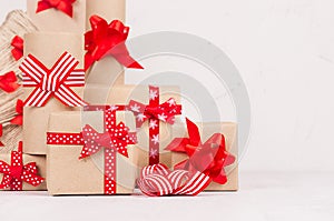 Handmade christmas gifts boxes of kraft paper, christmas tree with festive red ribbons and bows closeup on white wood background.