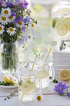 Handmade citrus limonade in jug with sliced lemon and mint decorate thyme and with flowers at the village