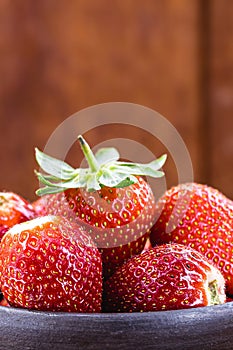handmade clay pot with Brazilian strawberries of the Albion variety, wooden background, copyspace