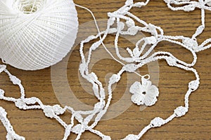 Handmade crochet white chain and a flower. Yarn ball for crochet or knitting on wooden table.