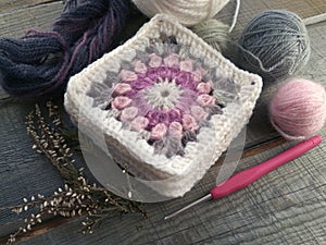 Handmade crocheting granny square, a hook and yarn balls