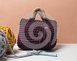 Handmade dark red and beige bag made with zpagetti yarn next to colored cloth balls