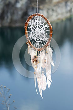 Handmade dream catcher with white doily on background of rocks and lake