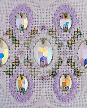 A handmade embroidery with white, purple and gold - green threads, beads and crystals on it